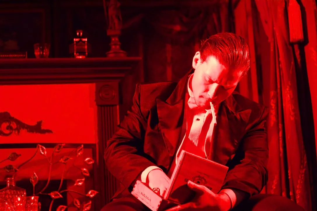 Nimrod Endvelt as Arthur Birling holding a book in a red lit scene